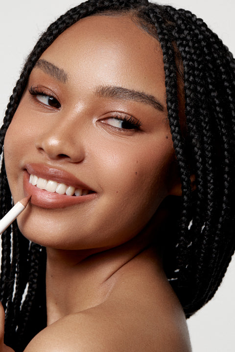 Woman with braided hair applying lip liner against a neutral background