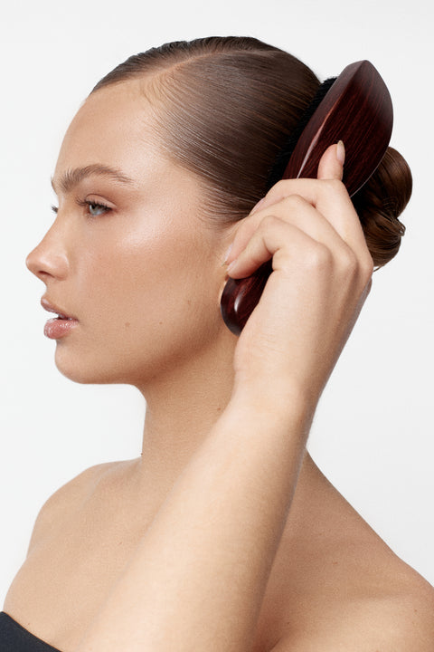 A woman with her hair neatly slicked back uses a Smoothing Brush, shown in profile against a clean white background.